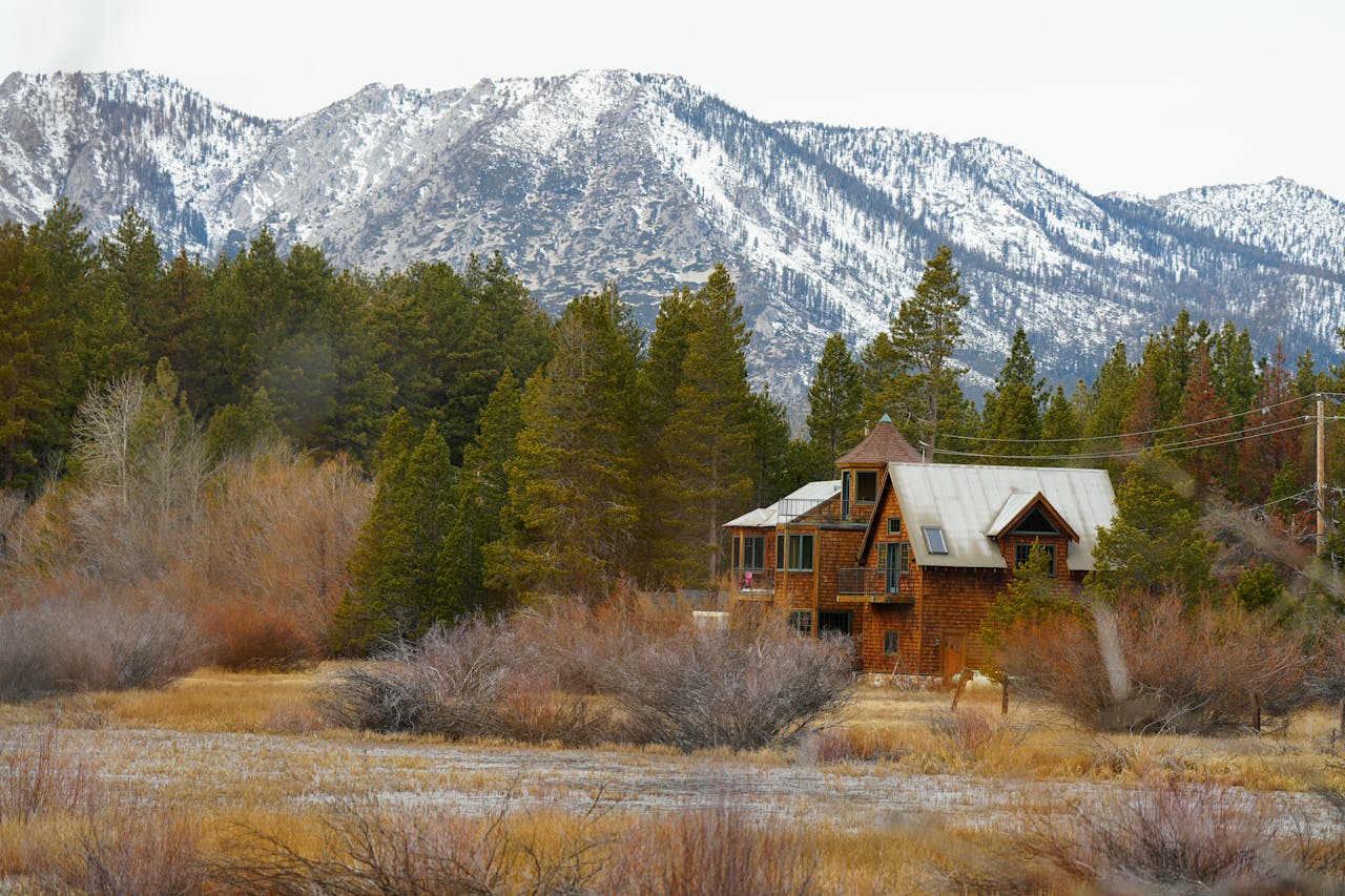 Rustic cabin nestled in serene snowy mountain scenery with woods surrounding.
